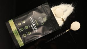 Flat lay of Origin Collagen collagen powder pouch with visible powder and measuring spoons on black background